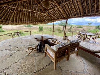 Eine gemütliche Terrasse mit Holzstühlen und einem Tisch aus Baumstamm, umgeben von einer weiten, grünen Landschaft.