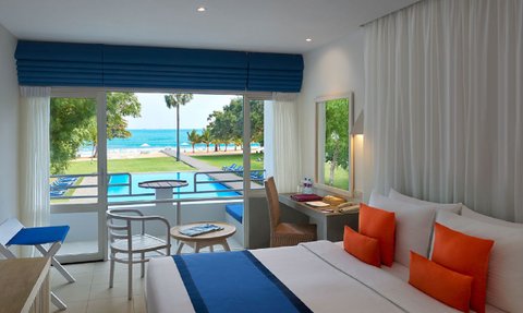 Ein helles Zimmer mit Meerblick, ausgestattet mit einem bequemen Bett und bunten Kissen, lädt zur Entspannung ein.