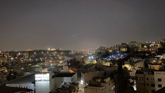 Die nächtliche Stadtansicht von Amman zeigt beleuchtete Gebäude und sanfte Hügel, die in der Dunkelheit schimmern.