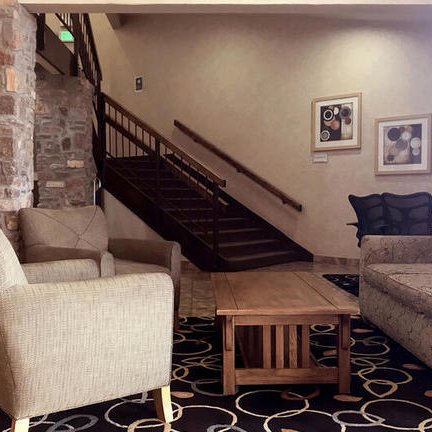 Der Empfangsbereich des Hotels zeigt eine gemütliche Sitzecke mit beigen Sesseln und einem Holztisch auf einem gemusterten Teppich.