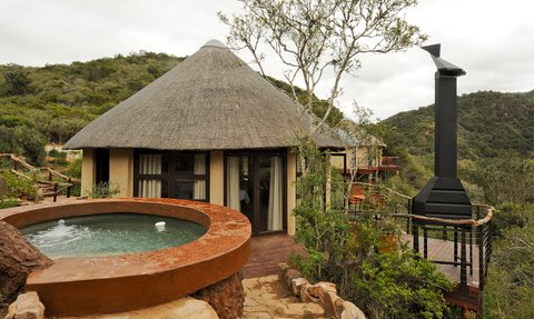 Ein traditionelles Rundhaus mit einem Strohdach, umgeben von üppiger Natur und einem kleinen Whirlpool im Vordergrund.