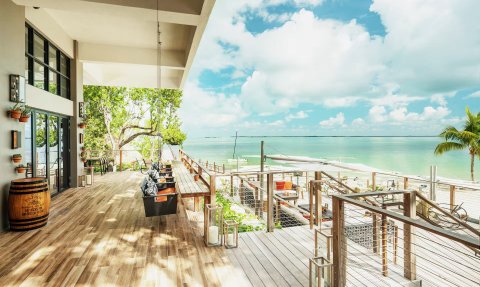 Eine großzügige Terrasse mit Holzbohlen bietet einen herrlichen Blick auf das glitzernde Wasser und den blauen Himmel.