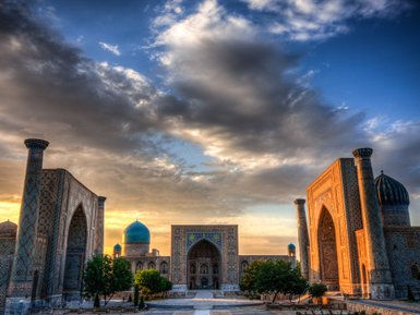 Die beeindruckende Architektur des Registan-Platzes in Samarkand wird von warmem Sonnenlicht beleuchtet, während Wolken vorbeiziehen.