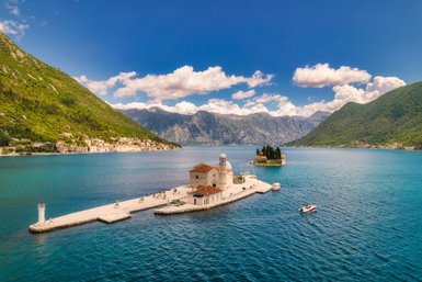 Eine malerische Küstenlandschaft mit einer kleinen Insel und einer Kirche, umgeben von Bergen und klarem Wasser.