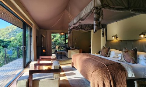 Ein elegantes Zimmer mit einem großen Bett, gemütlichen Sesseln und Blick auf die grüne Landschaft durch große Fenster.