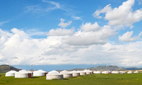 Eine weite Landschaft mit mehreren Jurten, umgeben von saftigem Grün und unter einem strahlend blauen Himmel.