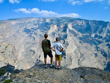Teenager und Kind blicken gemeinsam auf die atemberaubende Schluchtlandschaft des Jebel Shams – Oman mit Kindern