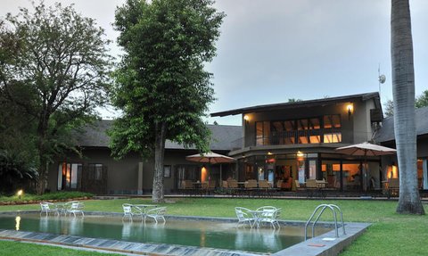 Ein modernes Lodge-Gebäude mit einem einladenden Pool und gemütlichen Sitzbereichen im Freien, umgeben von üppigem Grün.