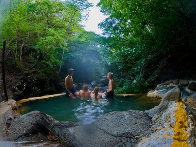 Gruppe von vier Personen in einem natürlichen Pool, umgeben von üppiger, grüner Vegetation in einem ruhigen Dschungelsetting.