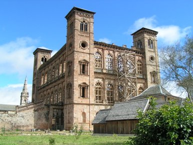 Die beeindruckende Ruine eines historischen Gebäudes mit großen Fenstern und einem markanten Turm unter einem blauen Himmel.