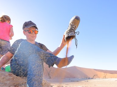 Ein Kind leert seinen Schuh aus, in dem sich Sand befindet - Namibia Rundreise mit Kindern