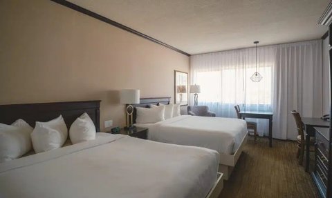 Ein modernes Hotelzimmer mit zwei großen Betten, eleganten Kissen und einem Schreibtisch neben einem großen Fenster.