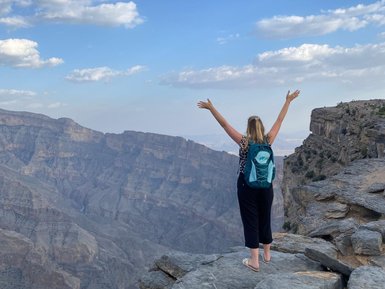 Frau steht auf einem Felsen und genießt die Aussicht über die Schluchten des Jebel Shams – Oman mit Kindern