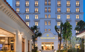 Ein elegantes Hotelgebäude mit dem Namen 'Ninh Binh Hidden Charm' strahlt in der Dämmerung, umgeben von üppigem Grün.