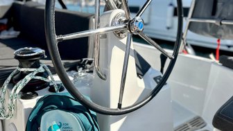 Das Steuerrad einer Yacht steht im Vordergrund, während ein Rucksack mit dem Aufdruck 'For Family Reisen' daneben liegt.