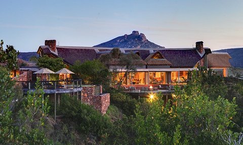 Eine malerische Lodge umgeben von üppigem Grün, mit einem beeindruckenden Berg im Hintergrund, der den Sonnenuntergang beleuchtet.
