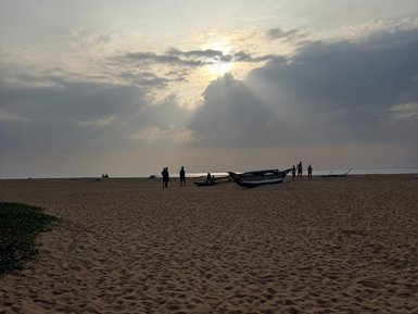 Am Strand von Negombo stehen Menschen vor einem dramatischen Himmel, während die Sonne durch die Wolken strahlt.