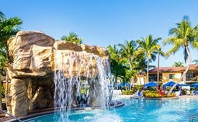 Ein malerischer Pool mit einem Wasserfall, umgeben von Palmen und Sonnenliegen, ideal für Entspannung und Erholung.