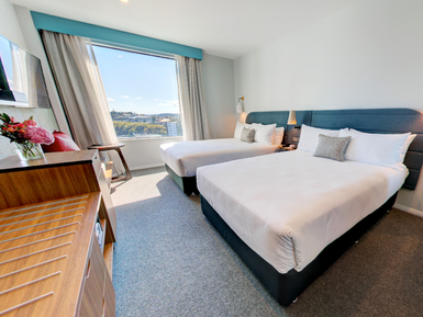 Ein modernes Hotelzimmer mit zwei Einzelbetten, großen Fenstern und einem Blick auf die Stadt Auckland.