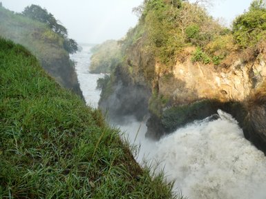 Ein beeindruckender Wasserfall stürzt in eine enge Schlucht, umgeben von üppigem Grün und nebligen Sprühnebel.