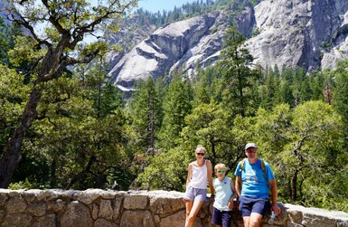Eine Familie steht an einer Steinmauer im Yosemite-Nationalpark, umgeben von hohen Bäumen und beeindruckenden Felsen.