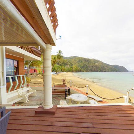 Ein Blick auf einen Strand mit sanften Wellen, umgeben von üppigem Grün und einem einladenden Holzdeck im Vordergrund.