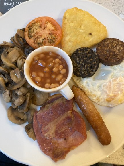 Ein traditionelles irisches Frühstück mit gebratenem Speck, Würstchen, Eiern und gebackenen Bohnen auf einem weißen Teller.