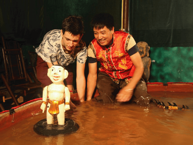 Zwei Männer beugen sich über einen kleinen Wasserpuppen, die in einem Becken schwimmt, und scheinen begeistert zu sein.