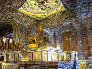 Ein prächtiger Raum mit einer goldenen Statue, umgeben von kunstvollen Wandmalereien und dekorativen Elementen.