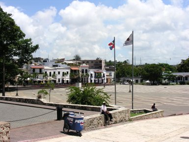 Ein ruhiger Platz in Santo Domingo mit historischen Gebäuden und einer Person, die auf einer Mauer sitzt und die Umgebung beobachtet.