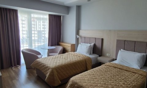 Zwei Einzelbetten mit goldenen Bettdecken in einem modernen Hotelzimmer, das viel Tageslicht durch große Fenster erhält.