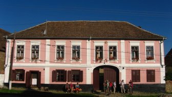 Ein charmantes, rosa gestrichenes Gästehaus mit blühenden Fenstern und einer einladenden Eingangstür, umgeben von Natur.