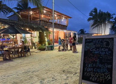 Eine Gruppe von Menschen steht vor einem Strandrestaurant, während die Dämmerung einsetzt und die Lichter leuchten.