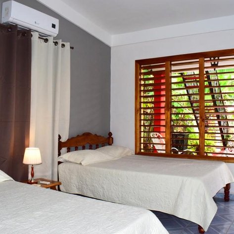 Ein helles Zimmer mit zwei Einzelbetten, einem Nachttisch und einem Fenster, das auf einen grünen Innenhof blickt.