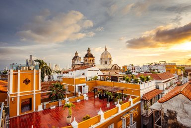 Die Aussicht auf Cartagena zeigt bunte Gebäude und historische Kirchen, während die Sonne am Horizont untergeht.