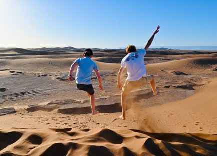 Kinder springen und haben Spaß auf den weiten Sanddünen der Sahara – Marokko Familienreise