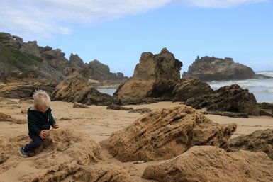 Kind klettert auf Felsen am Brenton Beach – Garden Route Reise mit Kindern