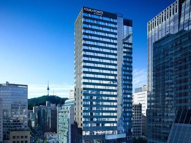 Das moderne Gebäude des Four Points Hotels in Seoul erhebt sich zwischen anderen Wolkenkratzern unter einem klaren blauen Himmel.