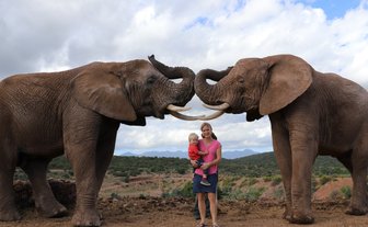 Mutter und Kind stehen lächelnd neben einem Elefanten in der Buffelsdrift Game Lodge – Garden Route mit Kindern