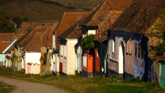 Eine malerische Straße mit bunten Häusern, die von sanften Hügeln umgeben ist, strahlt ländlichen Charme aus.