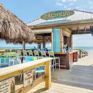 Ein einladender Strandbar mit Strohdach und bunten Stühlen, die zum Entspannen am Meer einladen.