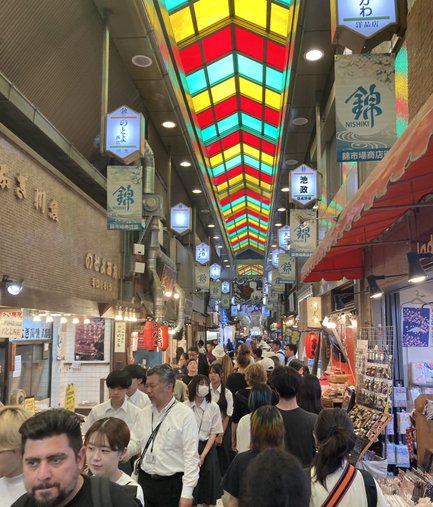 Ein belebter Markt in Kyoto mit bunten Lichtern und vielen Menschen, die durch die engen Gassen schlendern.
