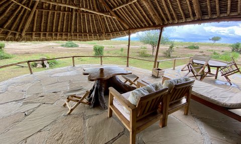 Eine gemütliche Terrasse mit Holzstühlen und einem Tisch aus Baumstamm, umgeben von einer weiten, grünen Landschaft.