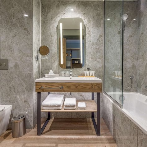 Ein modernes Badezimmer mit eleganten grauen Fliesen, einem Holzwaschtisch und einer großen Dusche aus Glas.