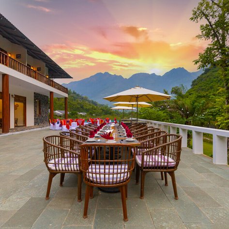 Ein eleganter Essbereich im Freien mit Blick auf die Berge, umgeben von üppigem Grün und einem atemberaubenden Sonnenuntergang.