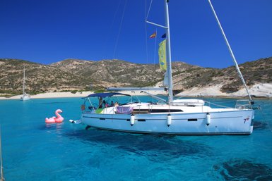 Ein Segelboot schaukelt sanft auf dem klaren, blauen Wasser, während ein pinker Flamingo-Schwimmring daneben schwimmt.