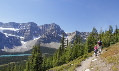 Ein Wanderer und ein Kind erkunden einen malerischen Pfad in den Rocky Mountains, umgeben von majestätischen Bergen und Nadelbäumen.
