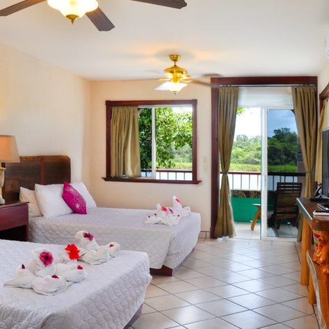 Ein helles Hotelzimmer mit zwei Betten, dekoriert mit Handtüchern in Form von Tieren und bunten Blumen auf den Betten.
