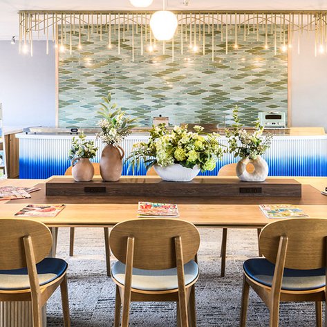 Ein stilvoller Lounge-Bereich mit einem großen Holztisch, umgeben von modernen Stühlen und dekorativen Blumenarrangements.