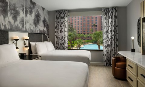 Helle Hotelzimmer mit zwei Einzelbetten, eleganten Möbeln und einer Aussicht auf einen Pool und Palmen durch das Fenster.